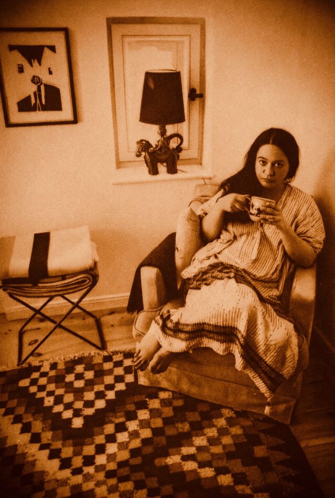 Bettina Indhivara on chair with cup in morning kaftan