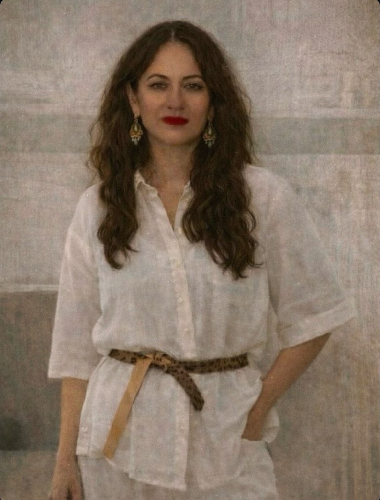 Woman in soft white outfit standing calmly in a warm painterly setting, representing gentle self-return and quiet composure