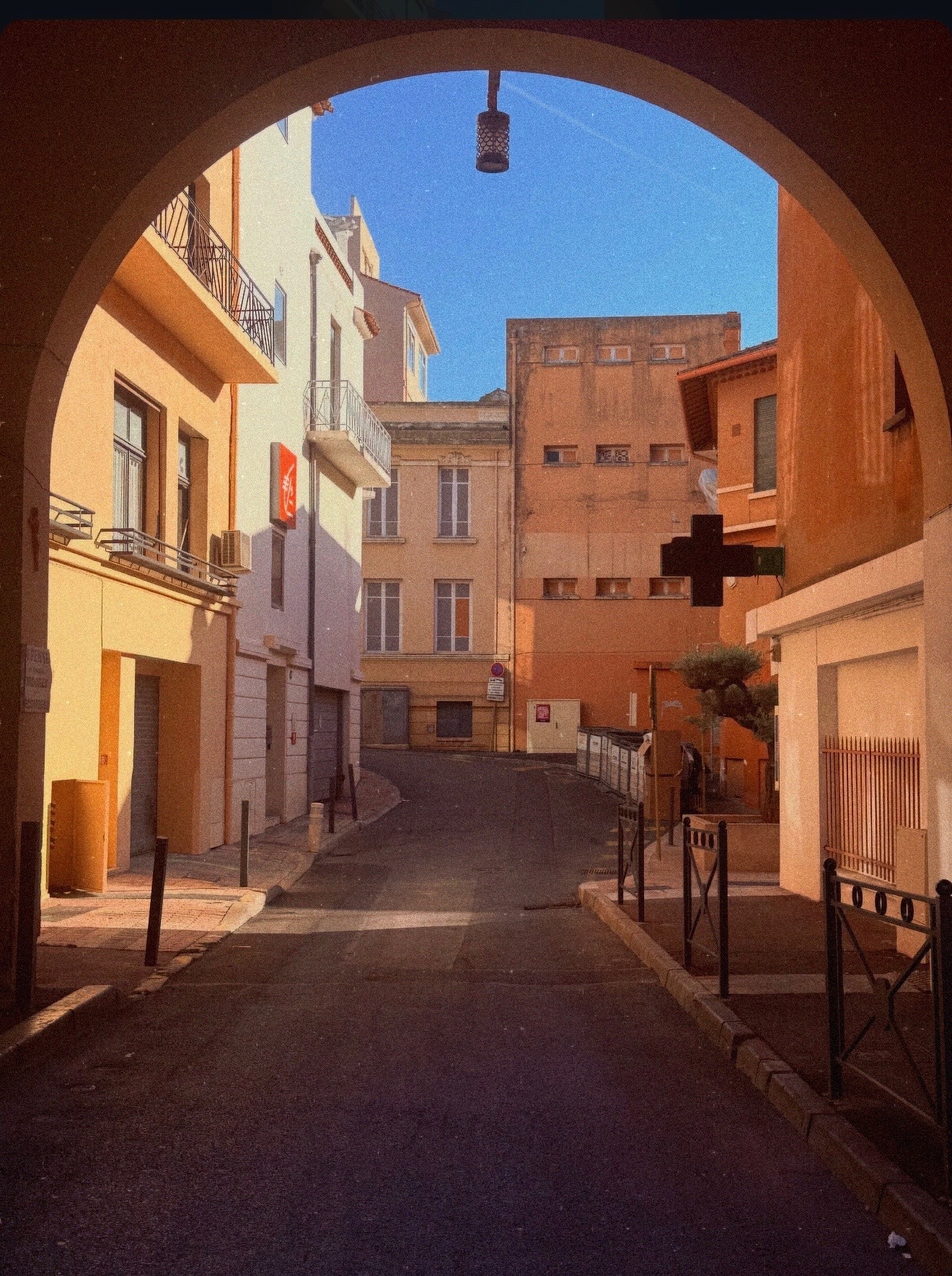 A quiet ochre-coloured street on the Côte d’Azur, seen through a shaded arch in the warm afternoon light.